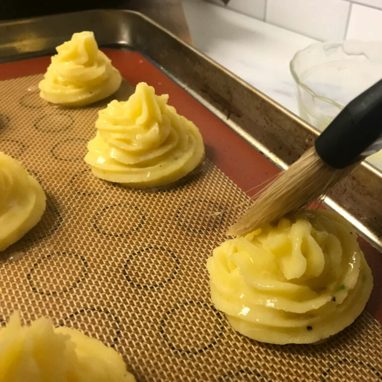 brushing butter on duchess potatoes.