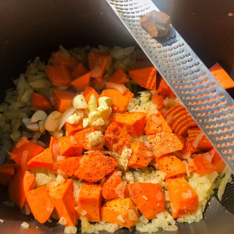 veggies cooking in pot with grater and nutmeg.
