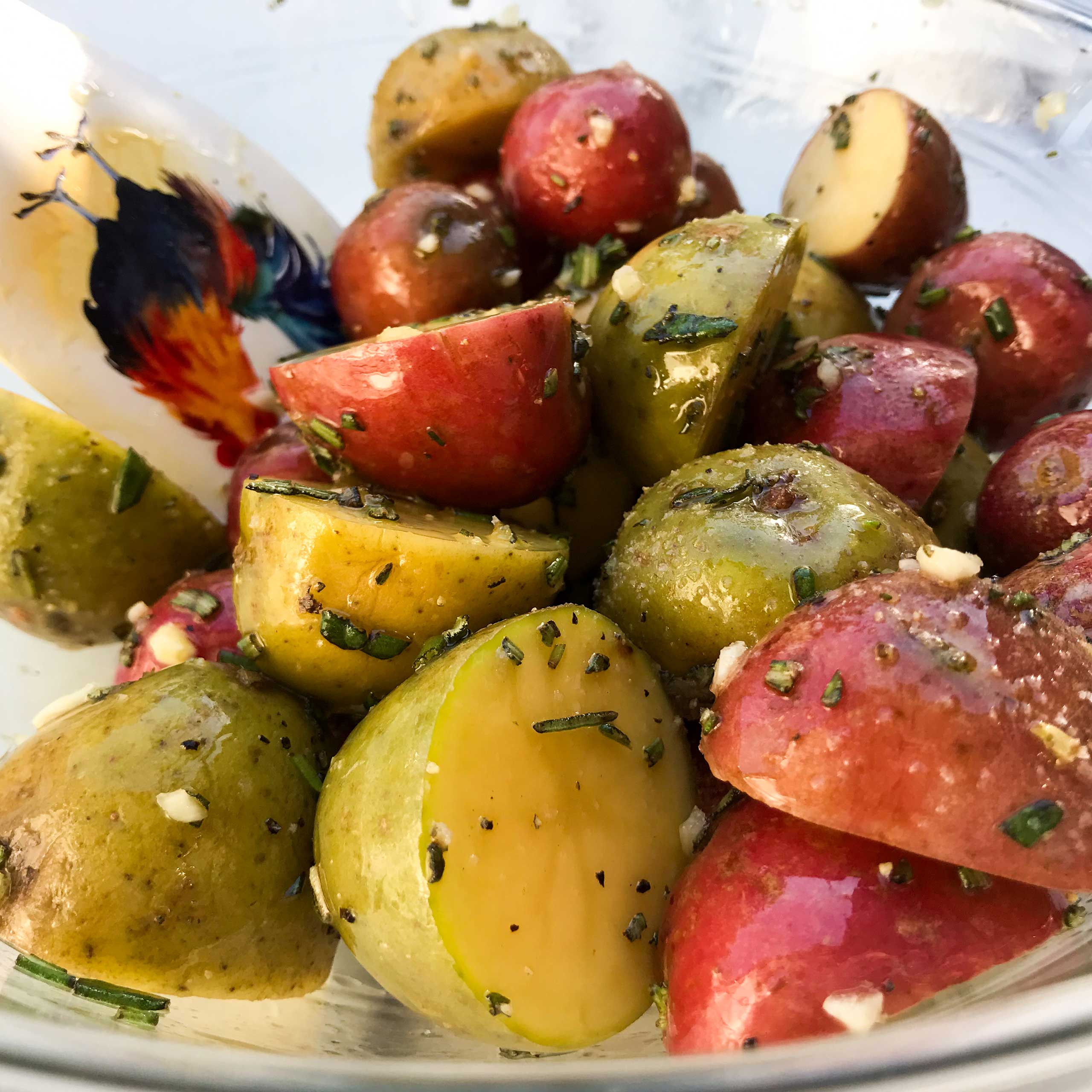 raw potatoes, rosemary and garlic tossed with olive oil in a bowl.