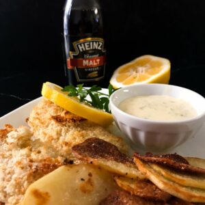 baked fish and garlic chips on a plate with tarter sauce and lemon.