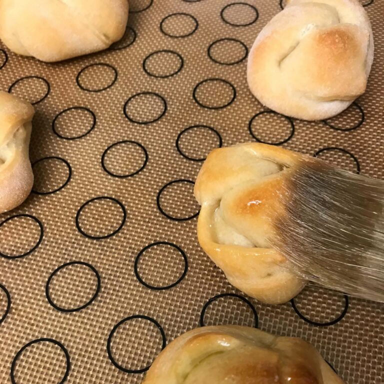 baked Garlic-Knots being basted with garlic oil.