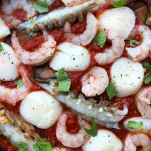 raw shellfish in marinara sauce in a skillet.