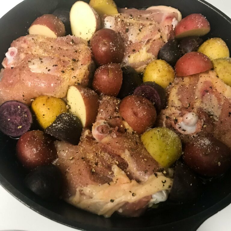 cast-iron skillet chicken with baby potatoes cooking in skillet.