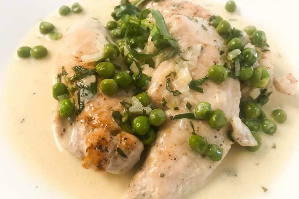 chicken tenders and peas with tarragon cream sauce on a plate.
