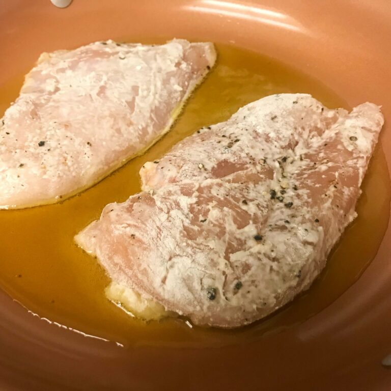 floured chicken cutlets in skillet.