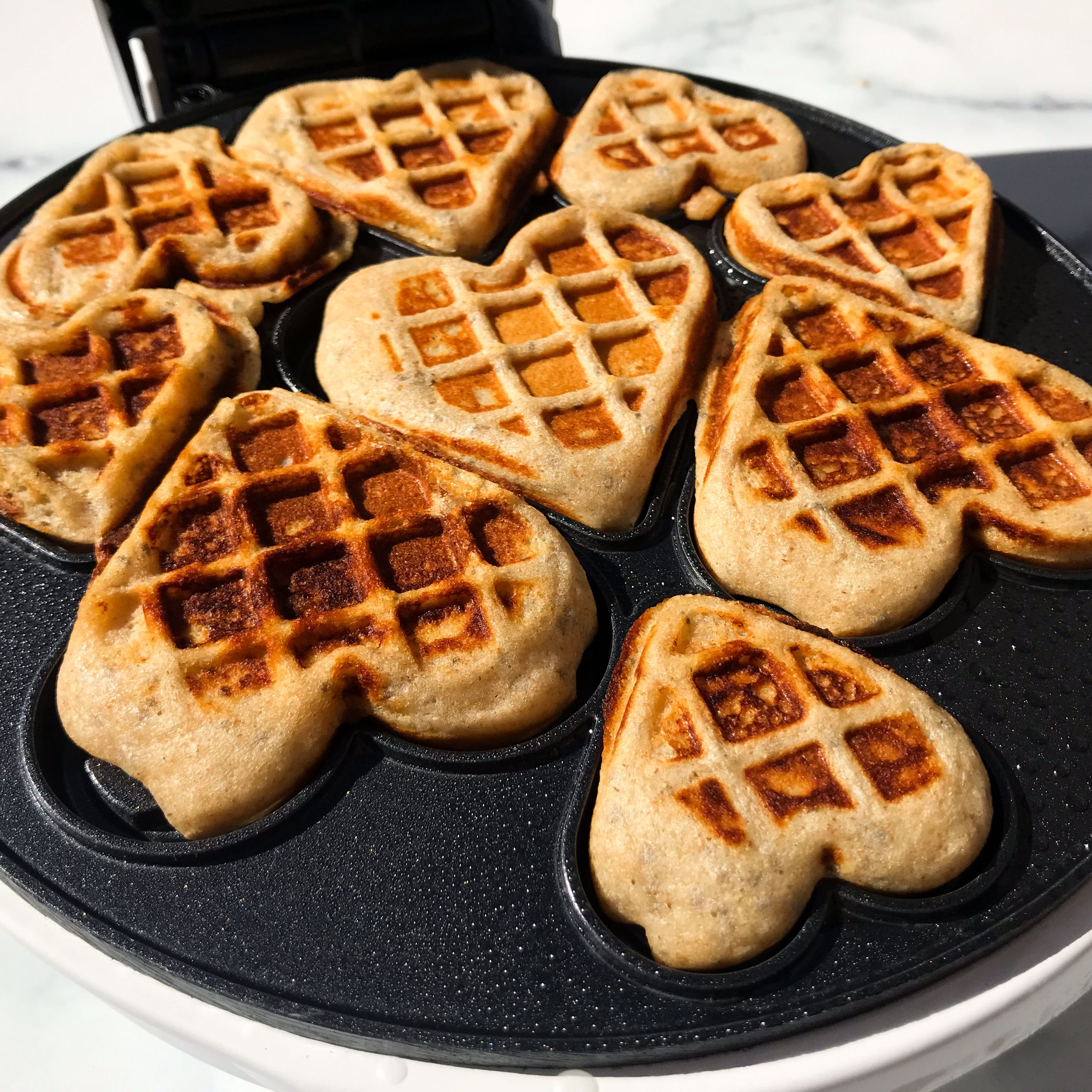cooked heart-shaped waffles in waffle maker.