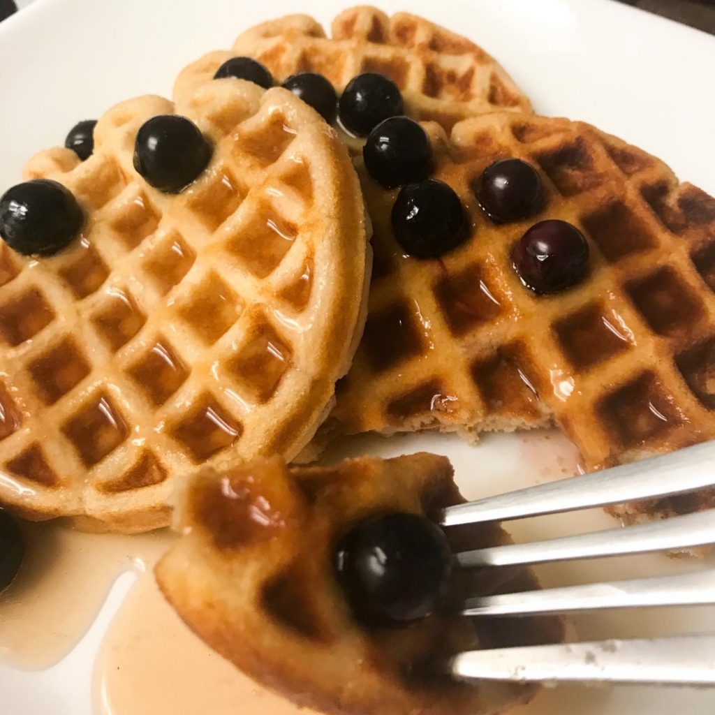 round shaped vanilla protein waffles on a plate with blueberries and syrup.
