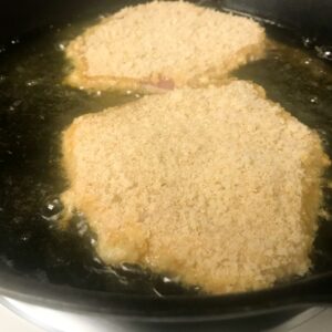 pork schnitzel frying in skillet.