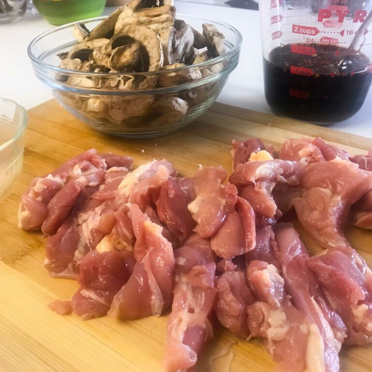 raw cut chicken, bowl of mushrooms and measuring cup of sauce.