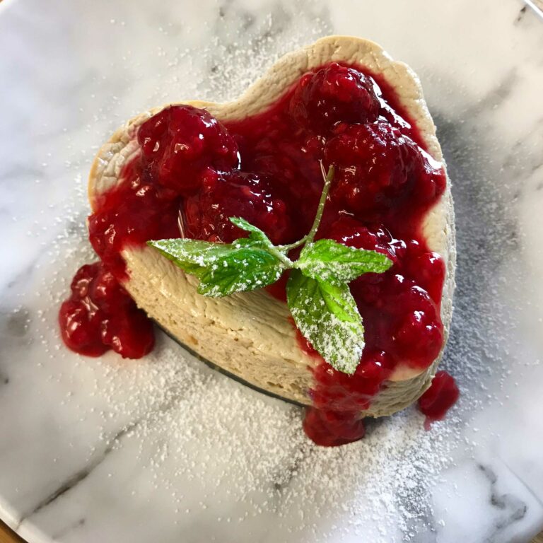 cheesecake topped with raspberry sauce, mint leaf and powdered sugar.