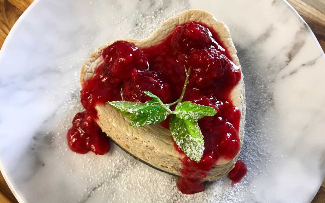 heart-shaped cheesecake topped with raspberry sauce, mint and powdered sugar.
