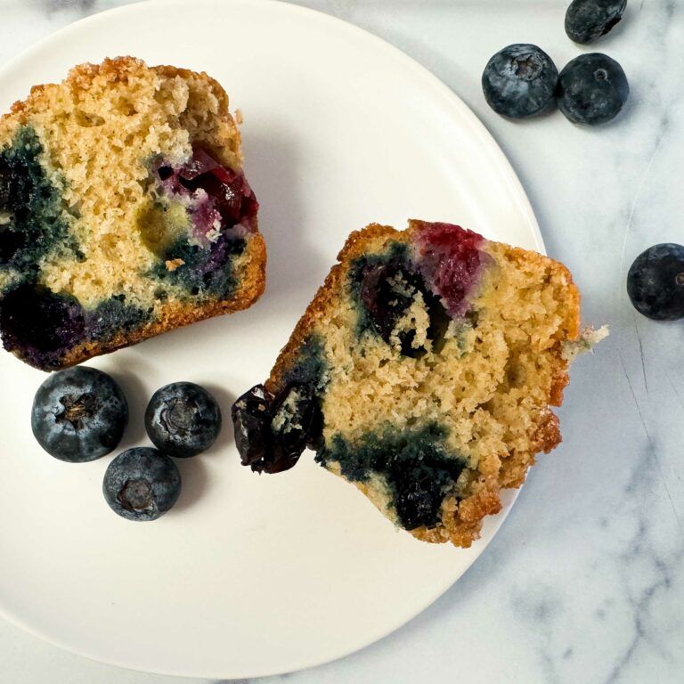 blueberry streusel muffin cut in half on a plate with fresh blueberries.