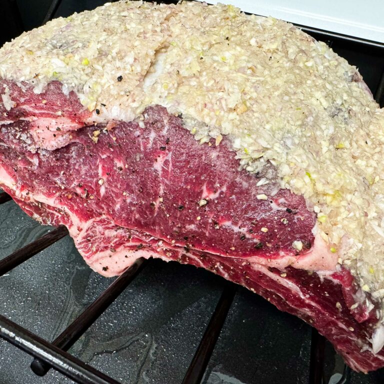 Raw rib roast covered in garlic and shallot crust sitting on a rack.