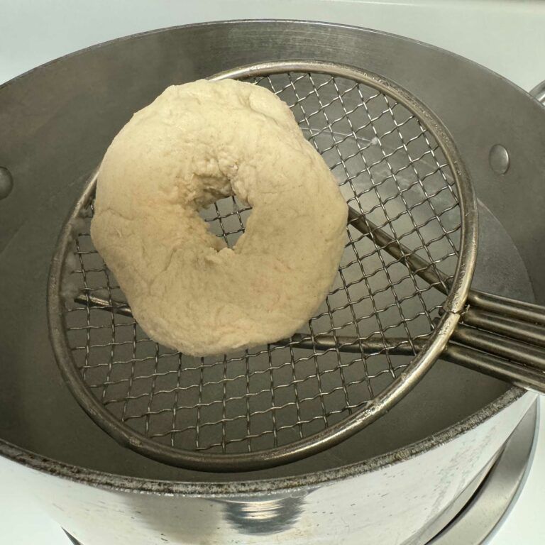 raw bagel on spider being put in boiling water.