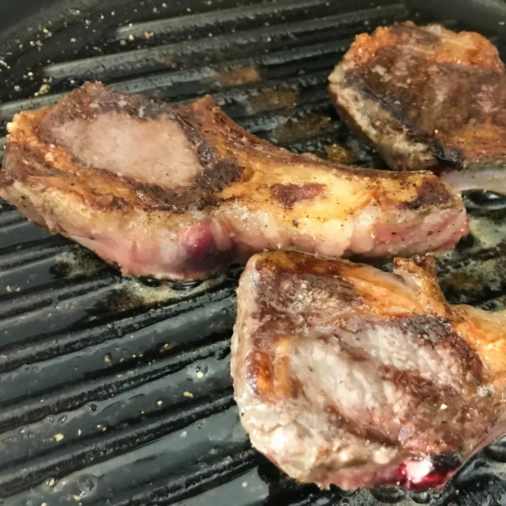 lamb chops cooking on a grill.