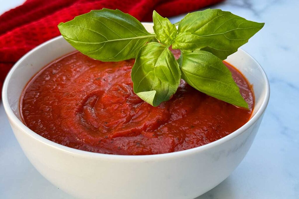 ny style pizza sauce in a bowl topped with basil.