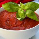 ny style pizza sauce in a bowl topped with basil.