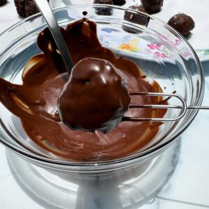 dipping a chocolate truffle in chocolate coating.