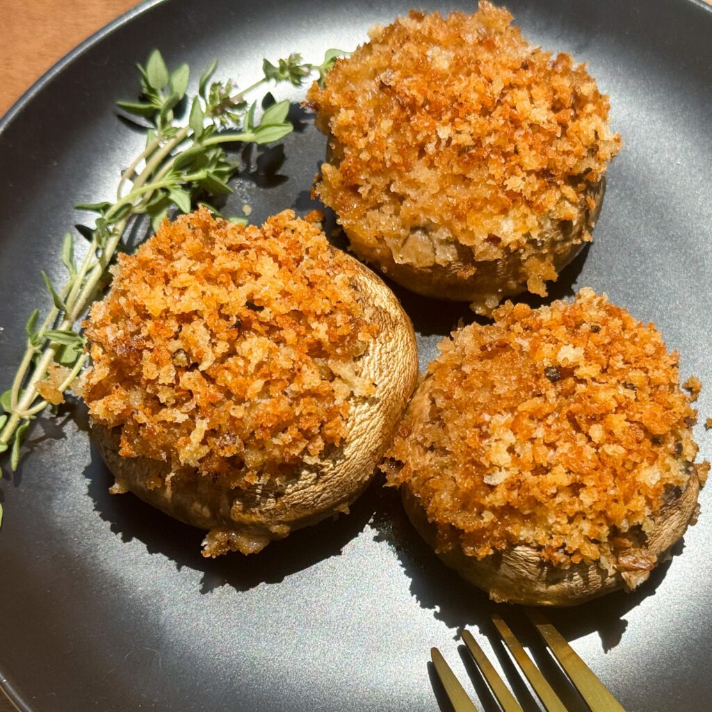 three stuffed mushrooms on a plate with thyme.