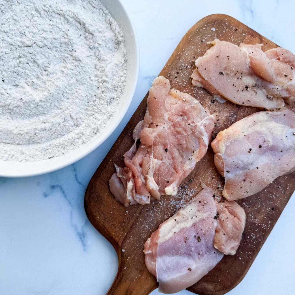 raw chicken next to bowl of flour mixture.