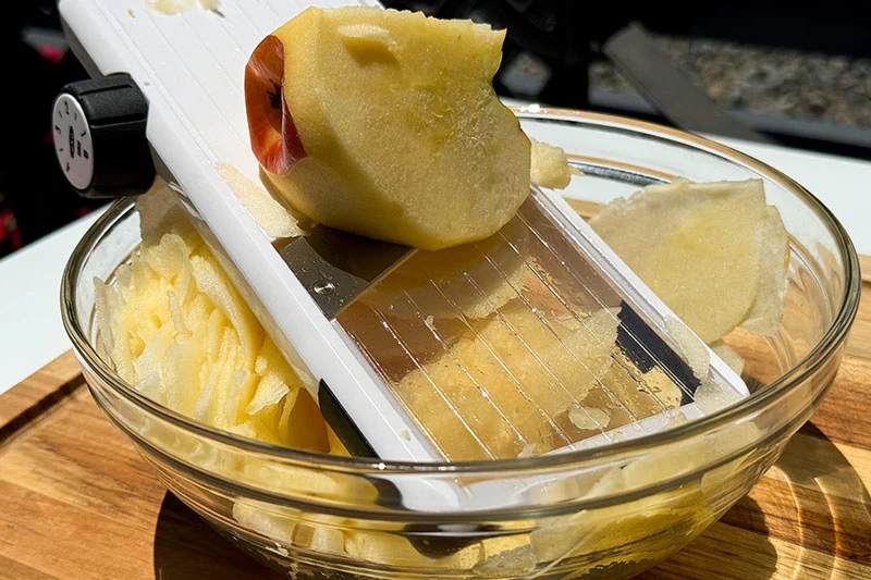 apple being sliced on a mandoline.