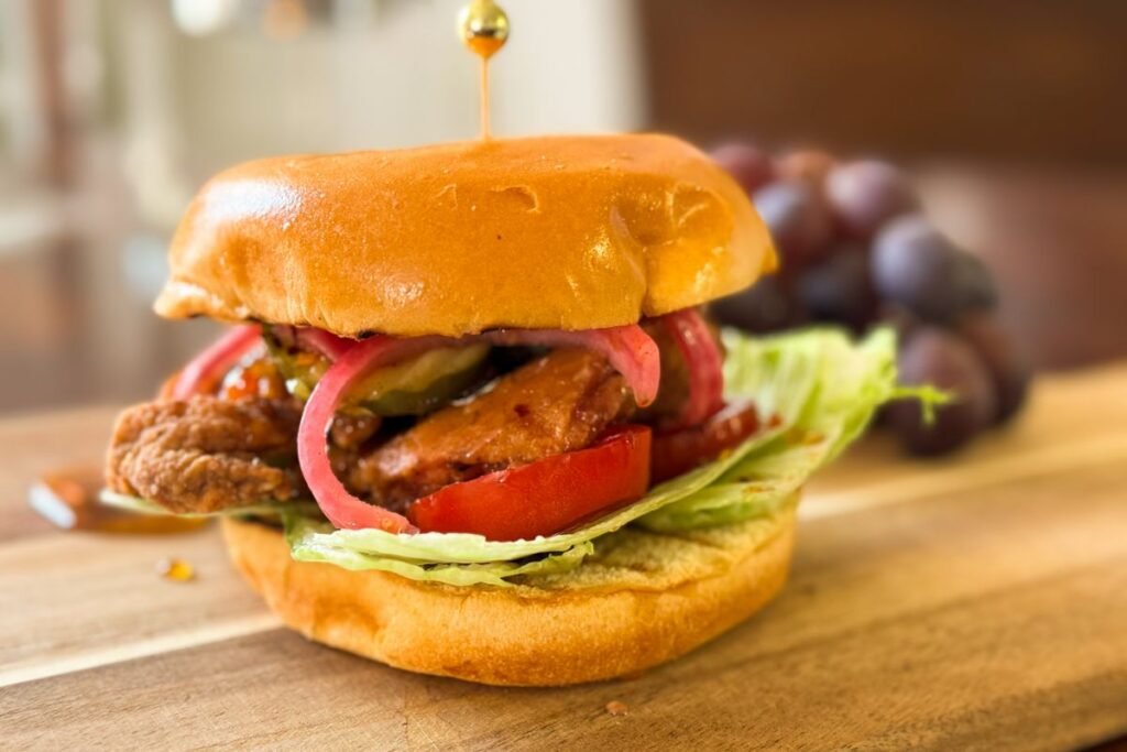 crispy chicken burger on a cutting board with grapes.