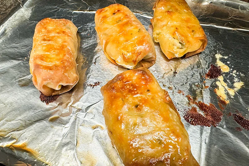 golden brown spring rolls on a baking sheet.