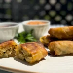 a cut spring roll on a plate with dipping sauces.