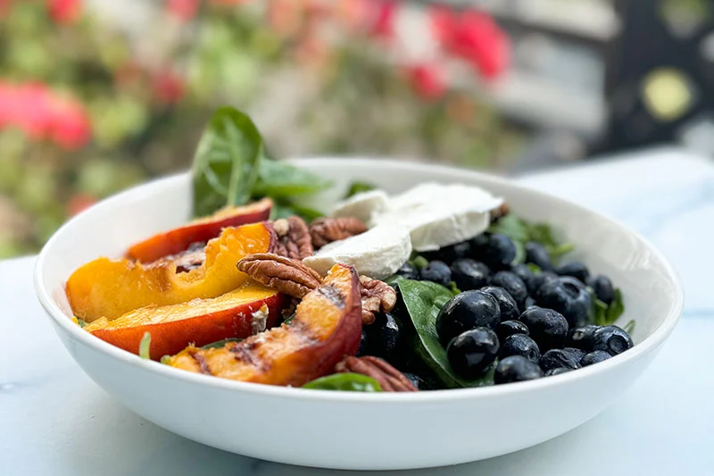 spinach salad with blueberries, goat cheese and grilled peaches in a bowl.