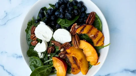 spinach salad with blueberries, goat cheese and grilled peaches in a bowl.