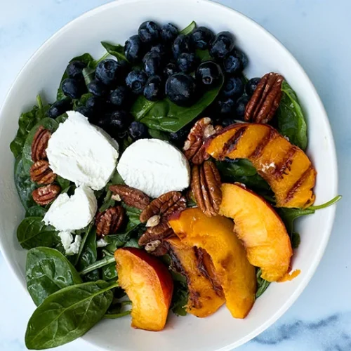 spinach salad with blueberries, goat cheese and grilled peaches in a bowl.