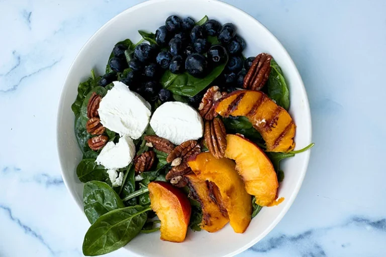 spinach salad with blueberries, goat cheese and grilled peaches in a bowl.