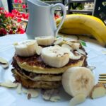 stack of almond flour pancakes with banana, almonds and syrup.