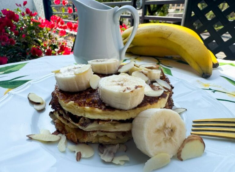 stack of almond flour pancakes with banana, almonds and syrup.