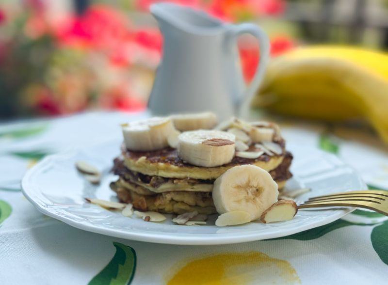 stack of pancakes with bananas, almonds and syrup.