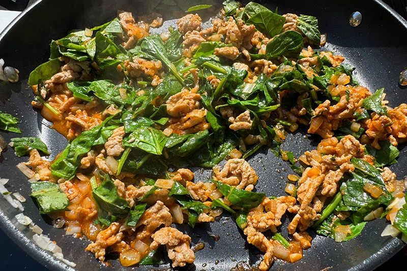 turkey and spinach cooking in skillet.