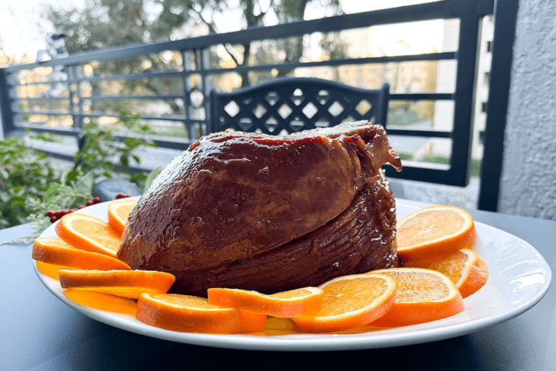 spiced marmalade glazed ham on a platter with sliced oranges.