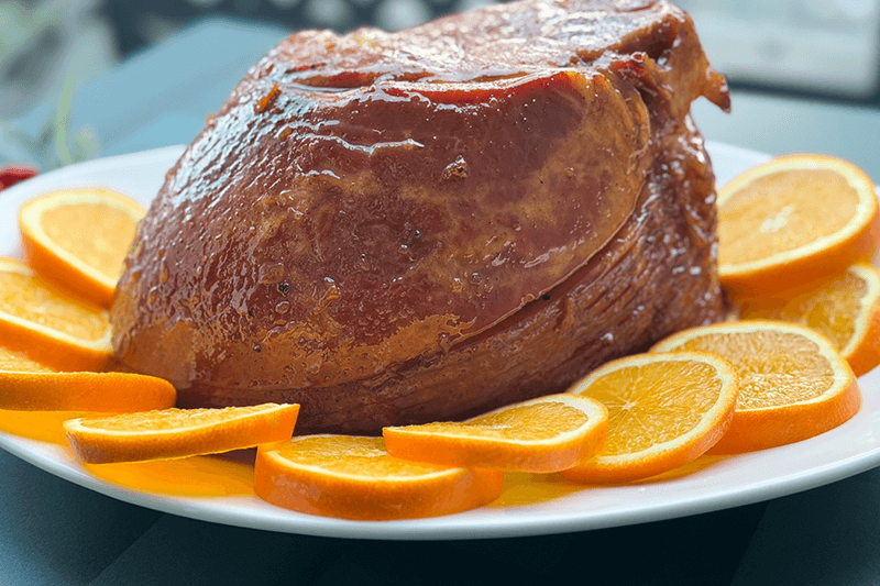 spiced marmalade glazed ham on a platter with sliced oranges.