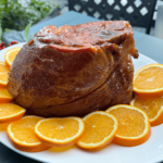 spiced marmalade glazed ham on a platter with sliced oranges.