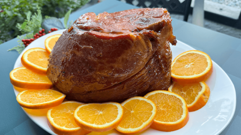 spiced marmalade glazed ham on a platter with sliced oranges.