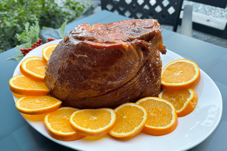 spiced marmalade glazed ham on a platter with sliced oranges.