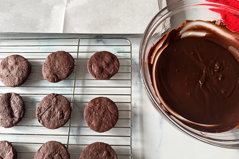 baked cookies on a rack next to a bowl of melted chocolate.