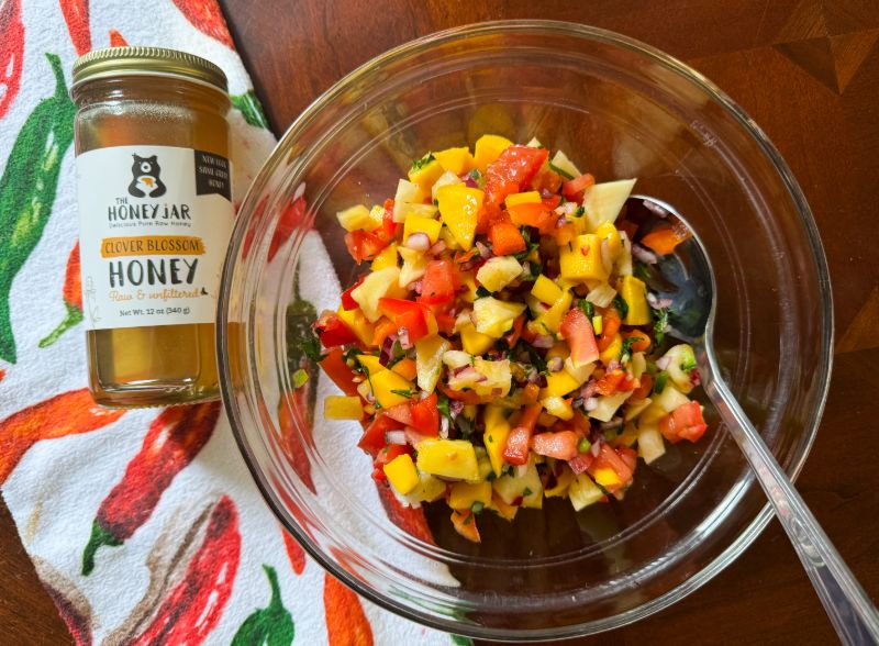 bowl of honey & lime pineapple and mango salsa with jar of honey.
