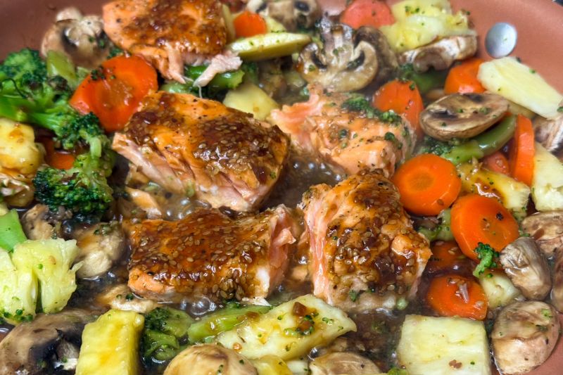 salmon broken into chunks cooking with veggies in teriyaki sauce.