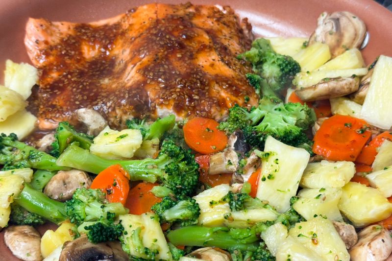 salmon and veggies in teriyaki sauce cooking in skillet.