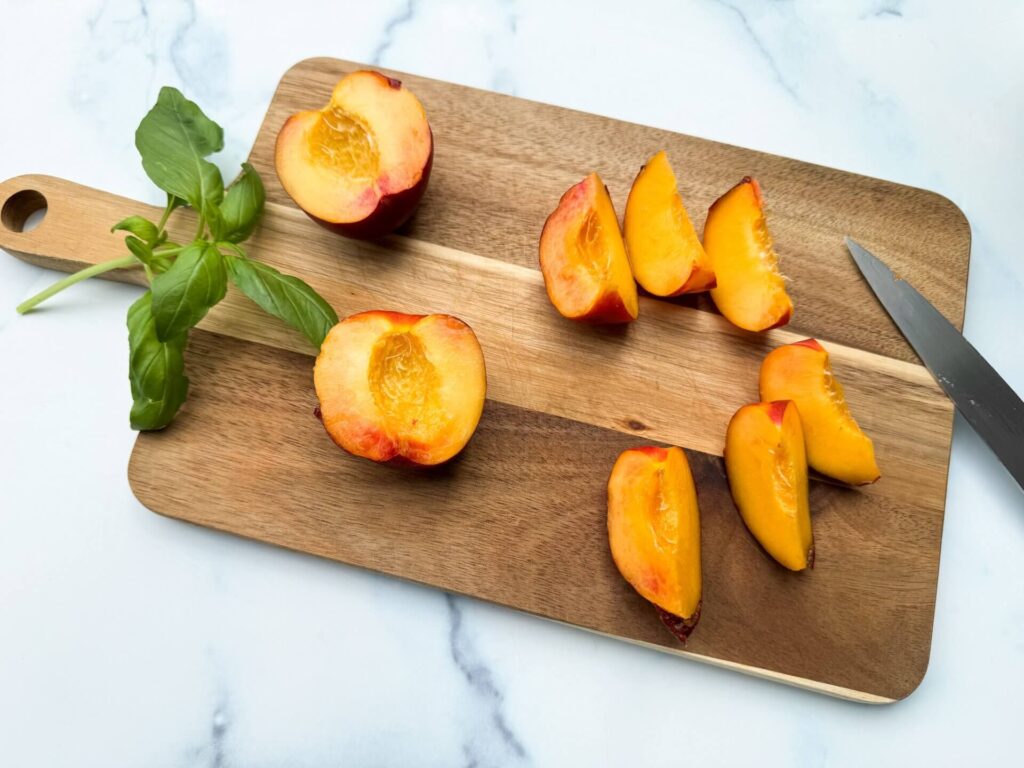 Fresh peaches on a wooden cutting board beside a sharp knife, ready for slicing or preparation.