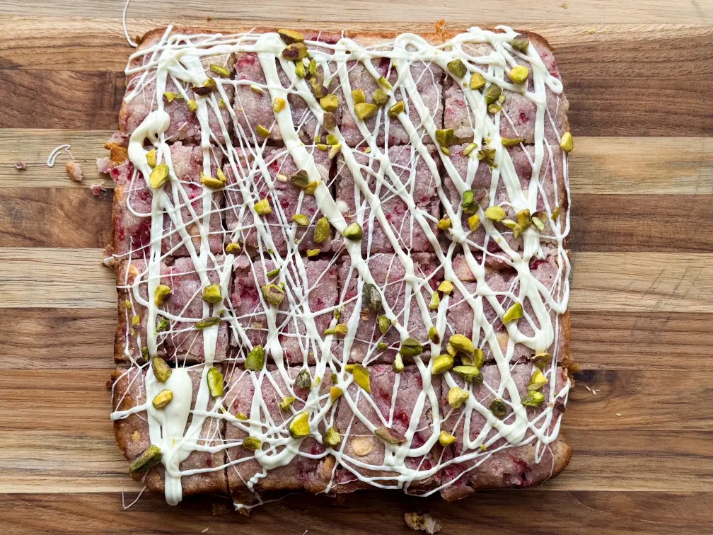 Raspberry white chocolate blondies, cut into squares, topped with white chocolate drizzle and pistachios.
