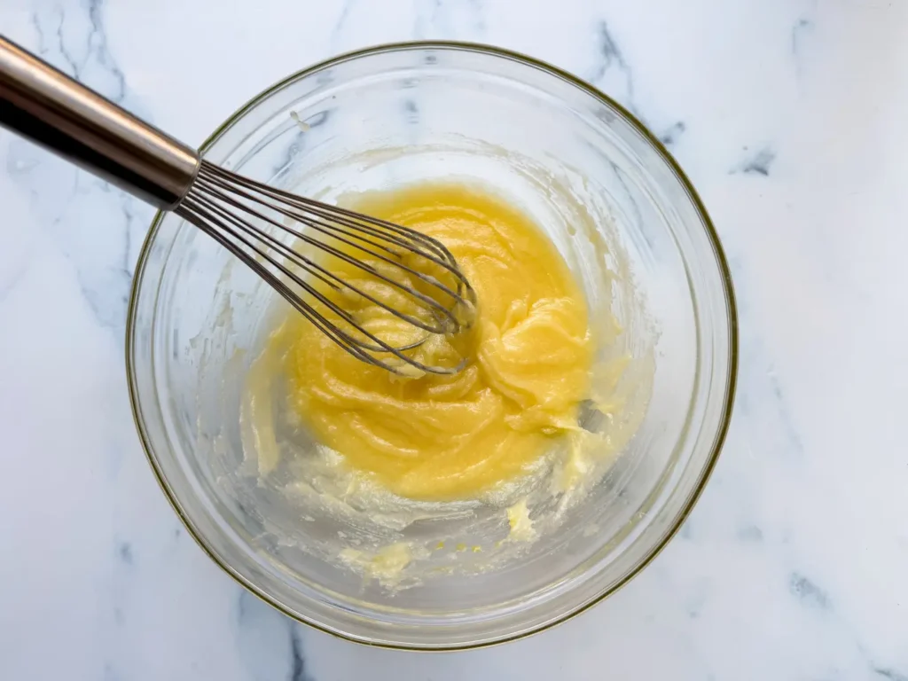 Whisk blending pale yellow batter in a glass bowl.