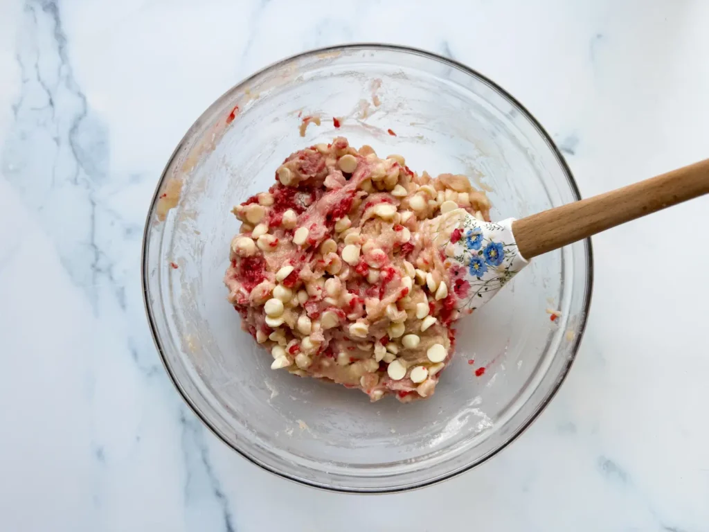 Glass bowl of raspberry white chocolate blonde cookie dough with spatula.