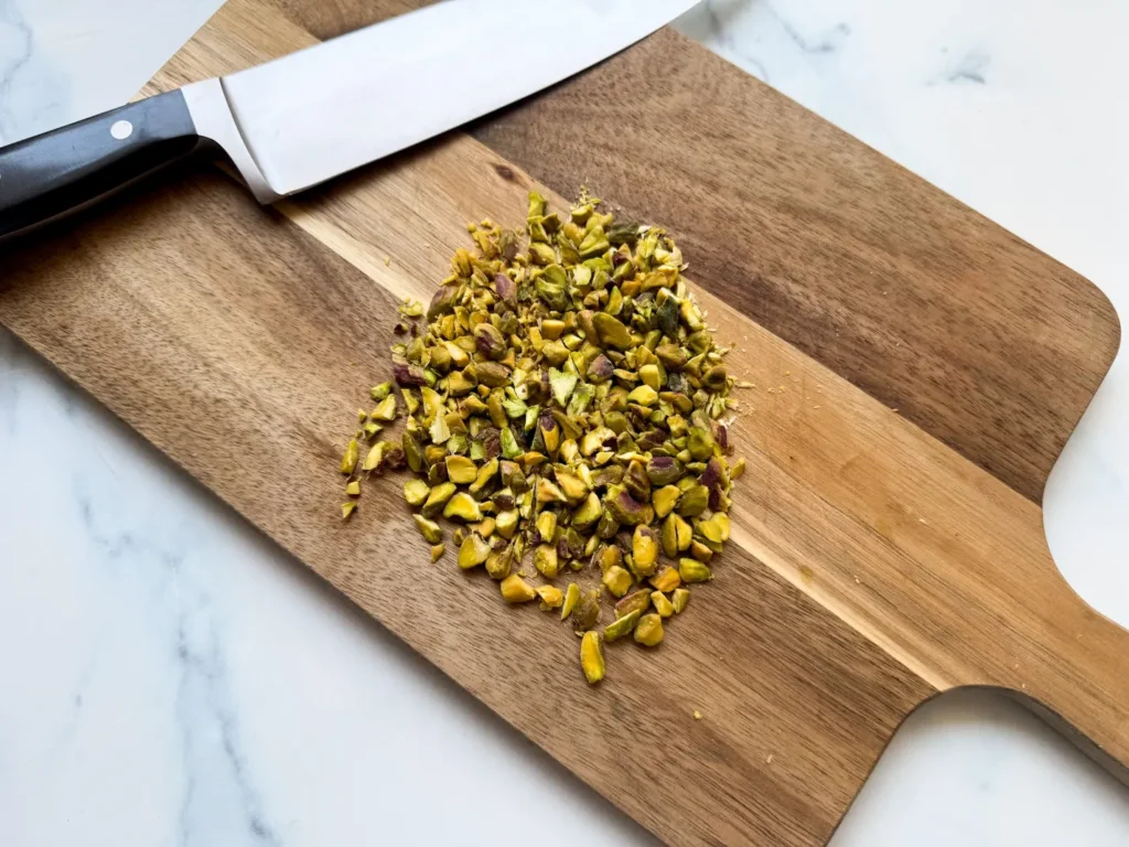Chopped pistachios on a wooden cutting board, next to a chef's knife.